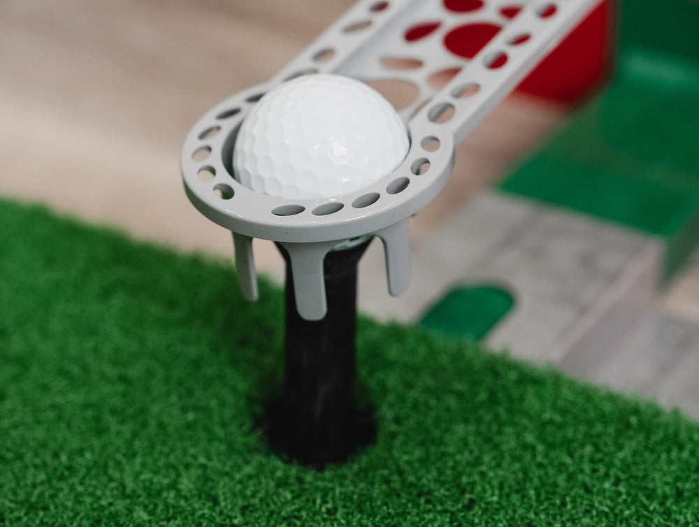 Golf ball on a tee with a golf simulator in the background